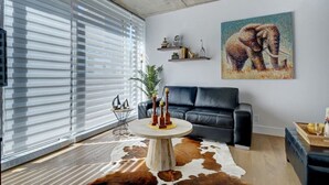 Una sala de estar moderna con un sofá de cuero negro, un tapiz de piel de vaca, una mesa de centro redonda con objetos decorativos, un cuadro abstracto grande y una planta.