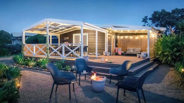 A covered outdoor seating area with chairs and a fire pit, surrounded by plants.