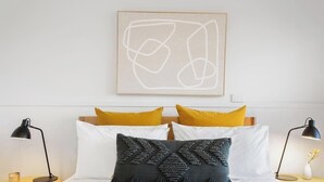 A bed with white and yellow pillows, a dark gray textured pillow, and two black desk lamps on either side.