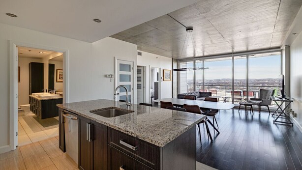 A modern kitchen with a large island, a dining area with a view, and a high ceiling. - Les Immeubles Charlevoix - 760415 (Ville de Québec)