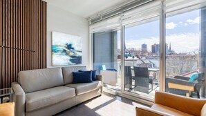 Una sala moderna con un sofá, sillas y un gran ventanal con vista a la ciudad.