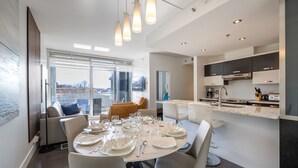 Un comedor moderno con una mesa redonda dispuesta para cuatro personas, un sofá y vistas a la ciudad.