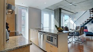 A modern kitchen with a central island, stainless steel appliances, and a dining area with a staircase. - Les Immeubles Charlevoix - 760506 (Ville de Québec)