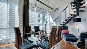 A modern dining area with a glass table, dark chairs, and a staircase with a black railing. - Les Immeubles Charlevoix - 760506 (Ville de Québec)