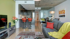 Ein modernes Wohnzimmer mit einer grauen Couch, roten Sesseln, einem Fernseher und einer Küche im Hintergrund.