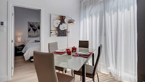 Una camera d'albergo moderna con zona pranzo, un tavolo in vetro, sottopiatti rossi e un quadro appeso al muro.