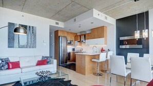 A modern living room with a white sofa, red cushions, a glass coffee table, and a red ottoman. - Les Immeubles Charlevoix - 760514 (Ville de Québec)