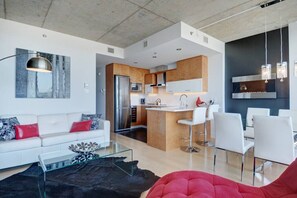 Een moderne woonkamer met een witte bank, rode kussens, een glazen salontafel en een rode poef.