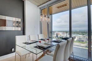 A modern dining area with a glass table and white chairs, large windows offering a city view, and a minimalist decor with a wooden ceiling and a wall-mounted light fixture. - Les Immeubles Charlevoix - 760514 (Ville de Québec)