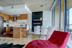A modern kitchen with wooden cabinets, a central island, and white bar stools. - Les Immeubles Charlevoix - 760514 (Ville de Québec)