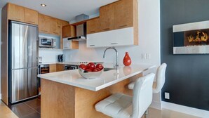 A modern kitchen with wooden cabinets, stainless steel appliances, and a central island with a bowl of red apples. - Les Immeubles Charlevoix - 760514 (Ville de Québec)