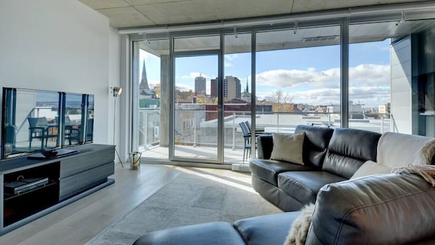 A modern living room with a large sliding glass door leading to a balcony, a leather sofa, and a flat-screen TV.