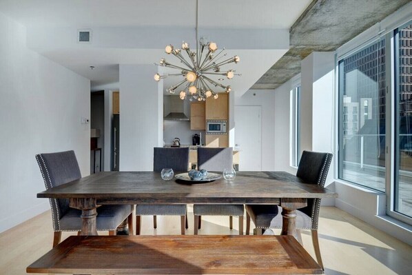 A modern dining area with a wooden table, four upholstered chairs, and a unique chandelier. - Les Immeubles Charlevoix - 760705 (Ville de Québec)
