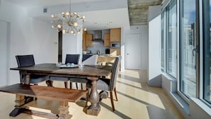 Een moderne eetruimte met een houten tafel en stoelen, een kroonluchter en een stadszicht door grote ramen.