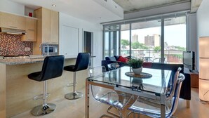 Eine moderne Küche mit Fliesenrückwand, Backofen und Mikrowelle. Ein Glastisch mit vier Stühlen, ein Topfpflanze und eine Couch mit Kissen sind ebenfalls vorhanden.