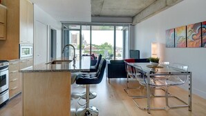 Eine moderne Küche mit einer großen Kochinsel, Barhocker, einem Esstisch mit Stühlen und Blick auf die Stadt durch große Fenster.