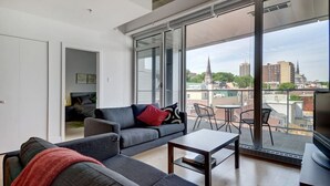 Ein modernes Wohnzimmer mit einem grauen Sofa, einem kleinen Tisch und einem Balkon mit Blick auf die Stadt.