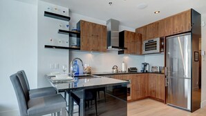 Une cuisine moderne avec des meubles en bois, un réfrigérateur en acier inoxydable et une table à manger en verre, accompagnée de chaises.