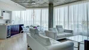 Una sala de estar moderna con una mesa de centro de vidrio, dos sofás blancos y un comedor con una mesa y sillas de vidrio.