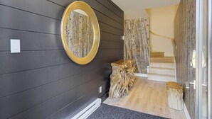 Un pasillo moderno con paredes de madera oscura, un espejo redondo y una escalera que sube a un piso superior.