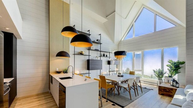 Una cocina moderna con una isla central, iluminación colgante y un comedor con un amplio ventanal.