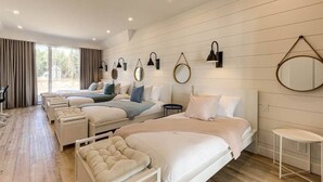 Habitación de hotel moderna con una cama grande, una cama más pequeña, un sofá y un escritorio. Hay varias lámparas y un espejo grande en la pared.