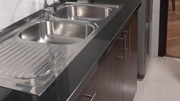 Une cuisine moderne dotée d’un évier en acier inoxydable, d’un réfrigérateur et de meubles de rangement en bois.