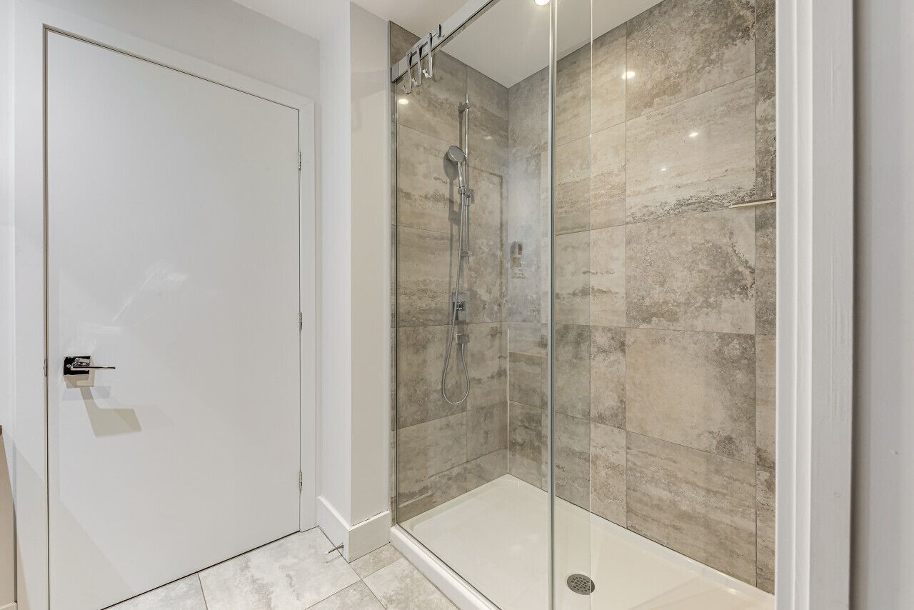 A modern bathroom with a glass-enclosed shower, marble tiles, and a white door.