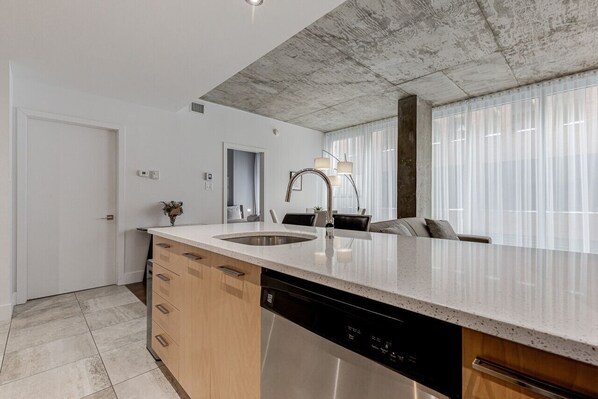 A modern kitchen with a large island, built-in dishwasher, and a dining area with a sofa and chairs.