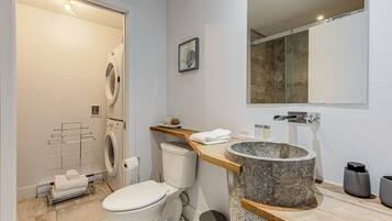 A modern bathroom with a built-in washing machine, a toilet, a large marble sink, and a mirror above the sink.