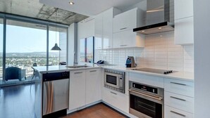 Une cuisine moderne avec des meubles blancs, des appareils en acier inoxydable et une grande fenêtre donnant sur la ville.