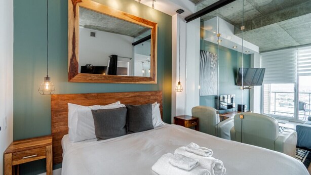 A hotel room with a large bed, a wooden headboard, a mirror, bedside lamps, a desk with a chair, and a TV. - Les Immeubles Charlevoix-Le 760631 (Québec)