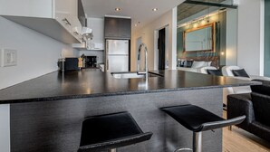 A modern kitchen with a central island, stainless steel appliances, and black bar stools. - Les Immeubles Charlevoix-Le 760631 (Québec)