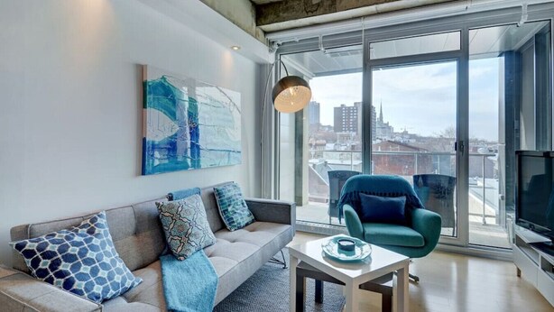 Ein modernes Wohnzimmer mit einer Couch, einem Sessel, einem Tisch und einem großen Fenster mit Blick auf die Stadt.