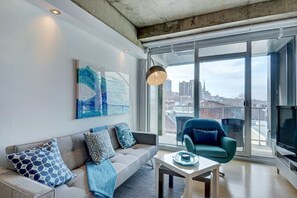 Ein modernes Wohnzimmer mit einer Couch, einem Sessel, einem Tisch und einem großen Fenster mit Blick auf die Stadt.