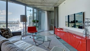 Una sala de estar moderna con una mesa de vidrio, un sillón rojo y un ventanal con vistas a la ciudad.