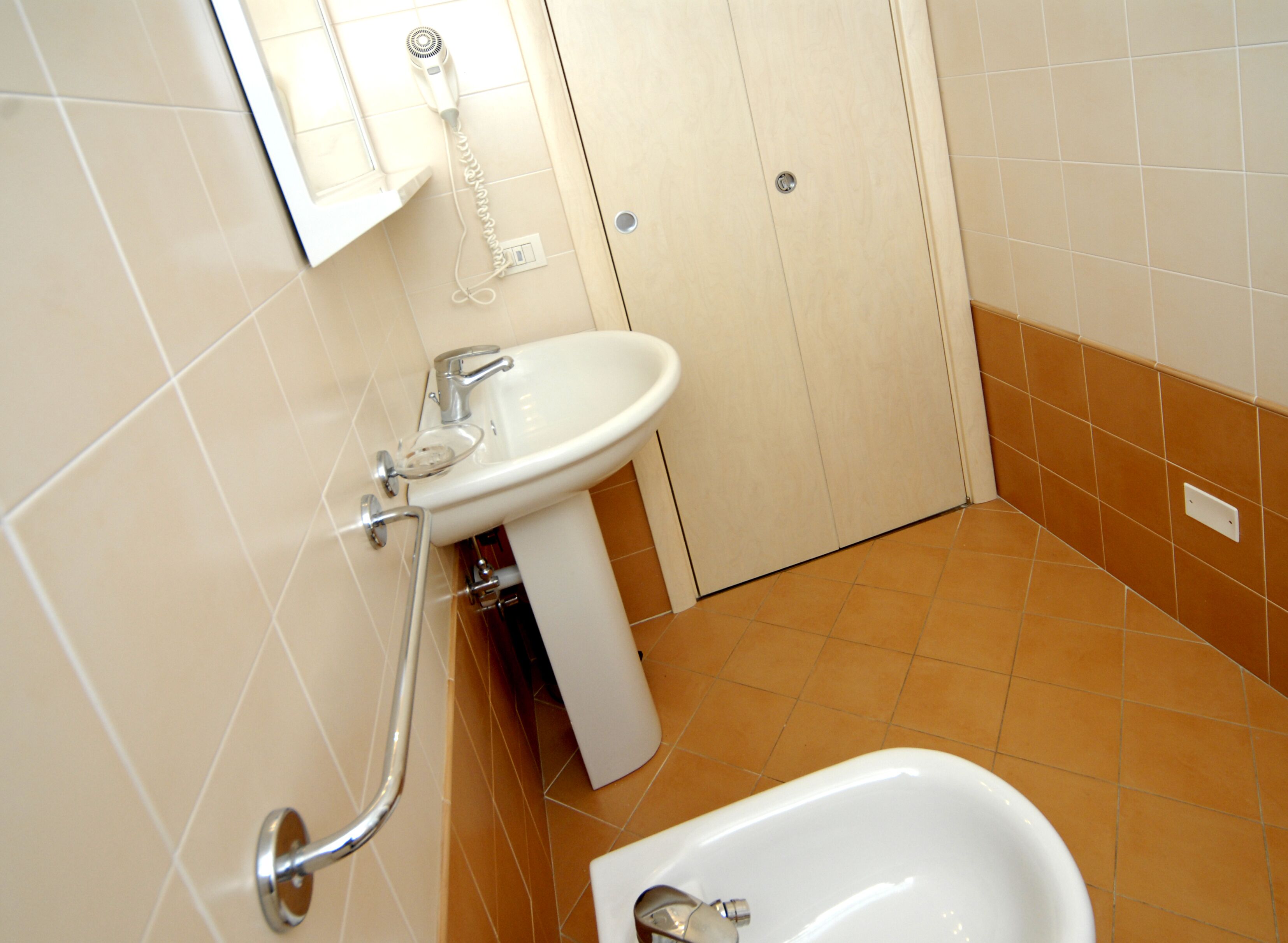 A bathroom with a white sink, a handheld hair dryer mounted on the wall, and a bathtub.