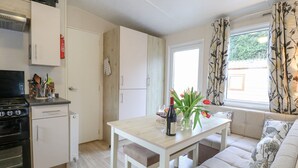 A compact kitchen with a stove, oven, and cabinets, a dining table with a vase of flowers, and a sofa with patterned cushions. - No 3 Foxburrow Hang (Great Yarmouth)