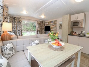 Una sala de estar acogedora con un sofá, una mesa con frutas y flores, y una cocina con armarios y un microondas.