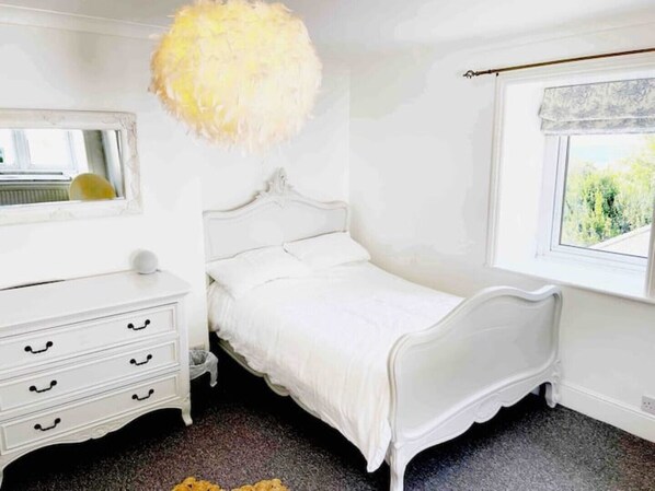 A white bedroom with a bed, dresser, and window.