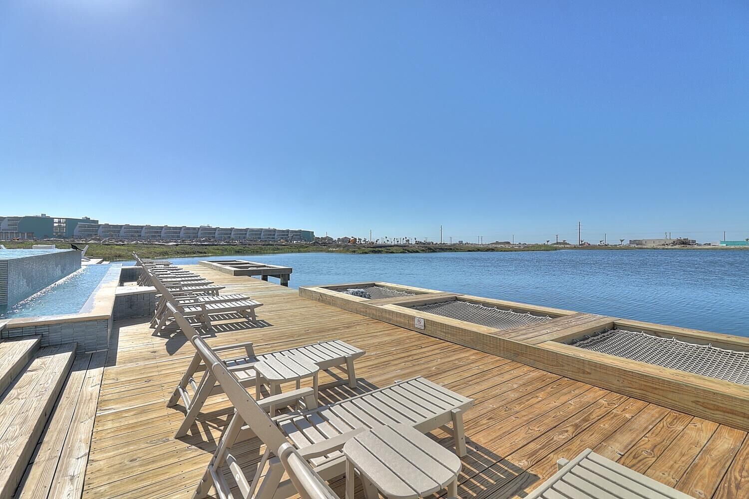A wooden deck with lounge chairs and a pool area overlooking a body of water.