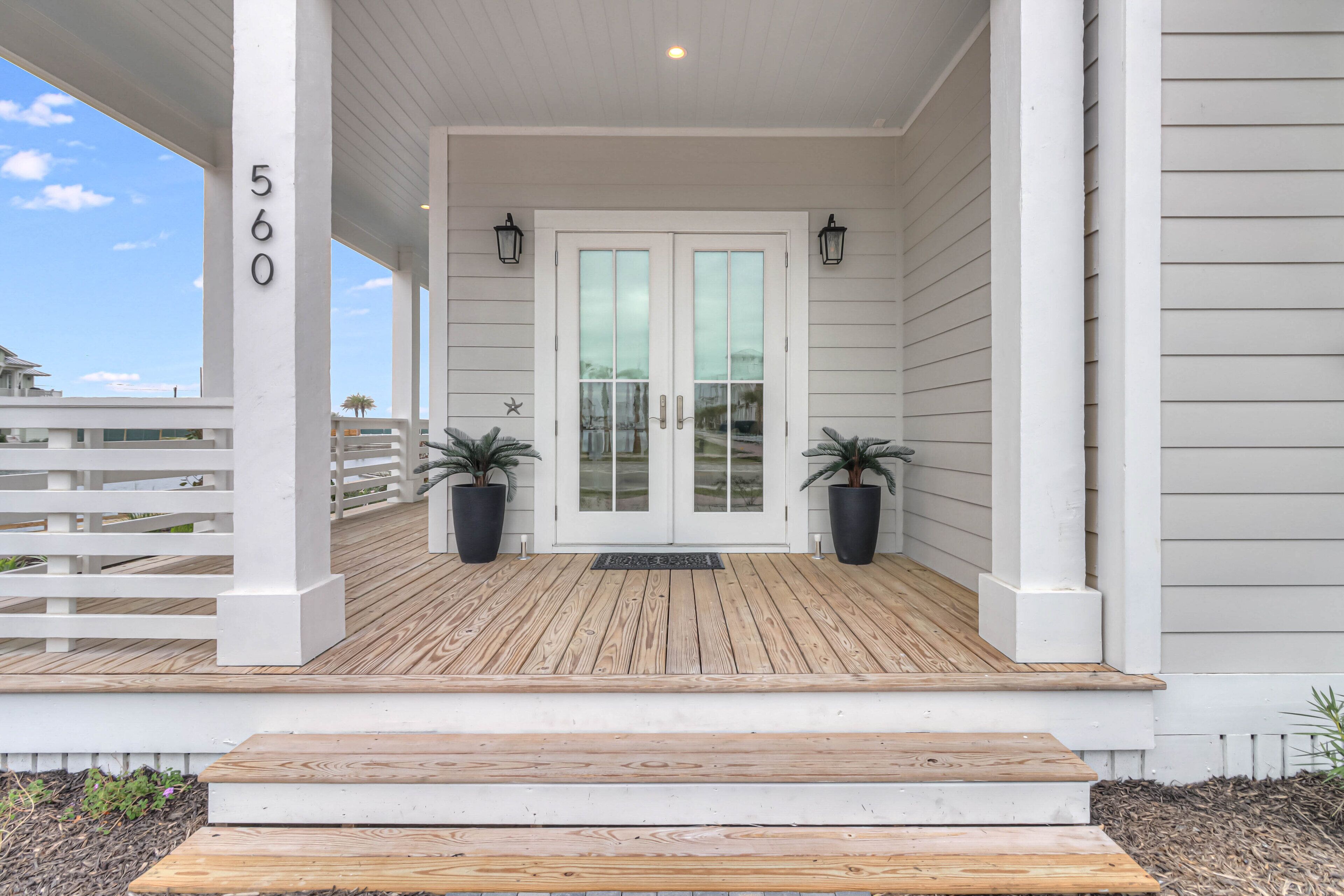 A wooden deck with a white railing, a double door with glass panels, and two potted plants.