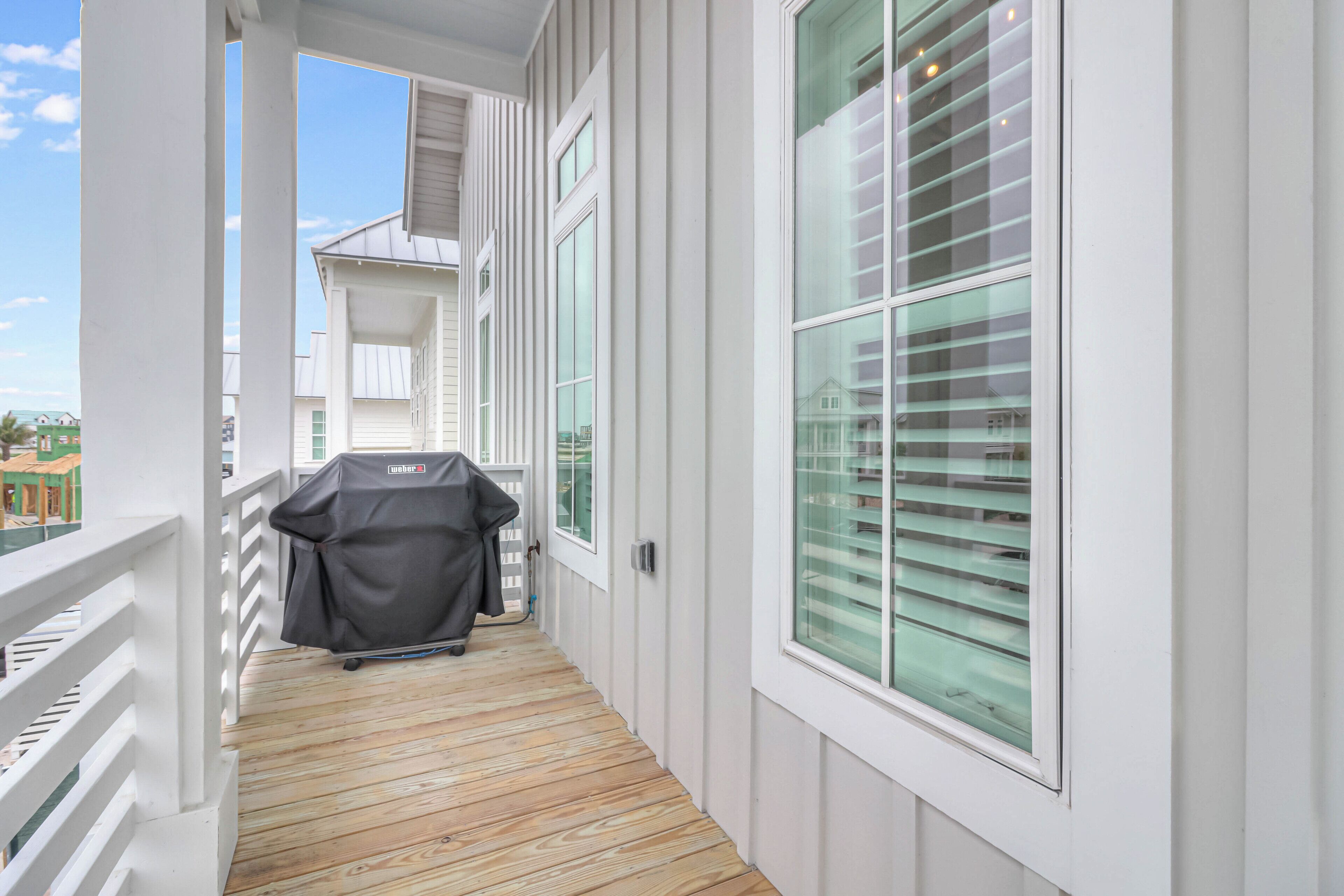 A covered wooden deck with a grill, white railings, and large windows with blinds.