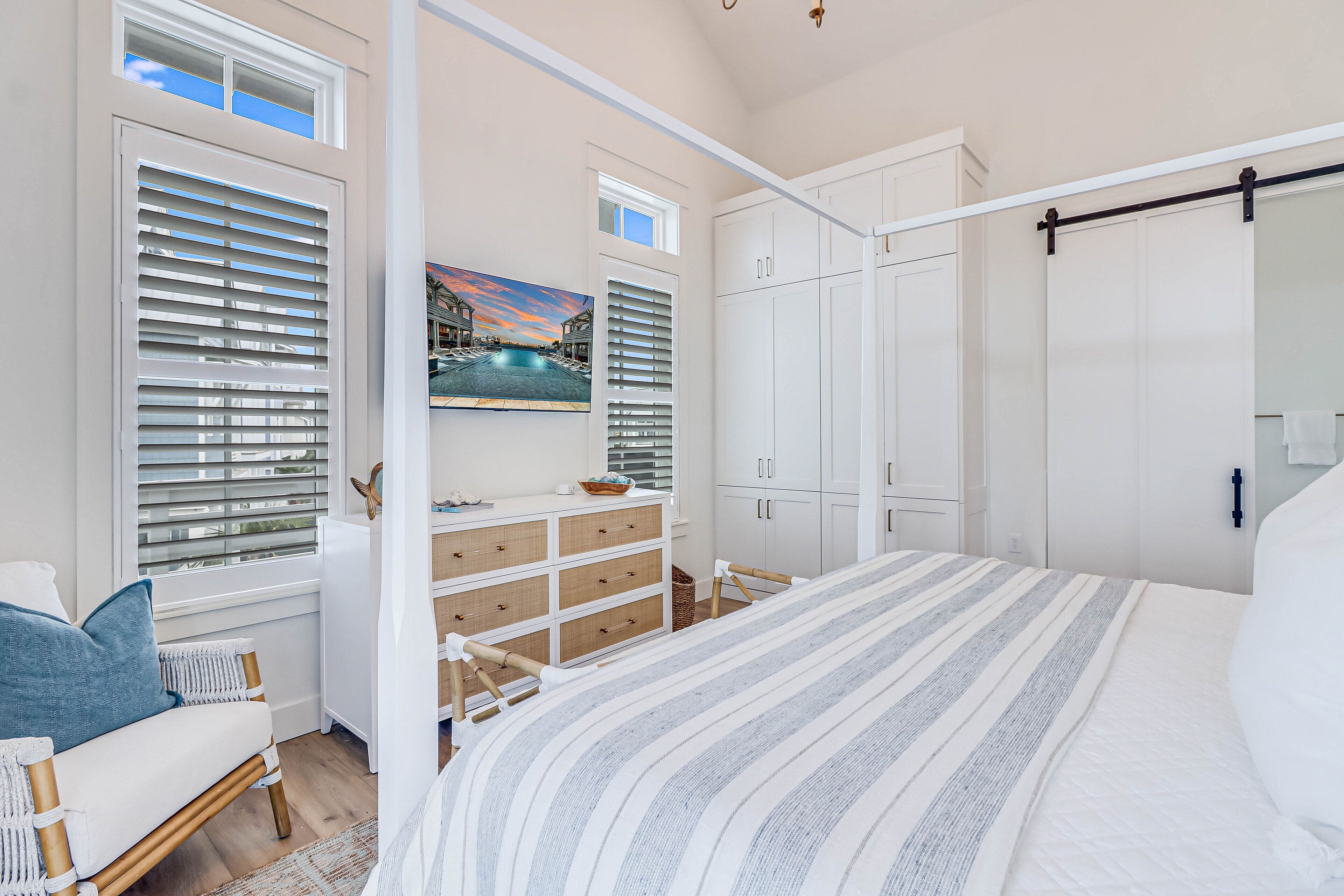 Une chambre à coucher avec un lit, une chaise en bois, une commode et un tableau représentant une piscine.