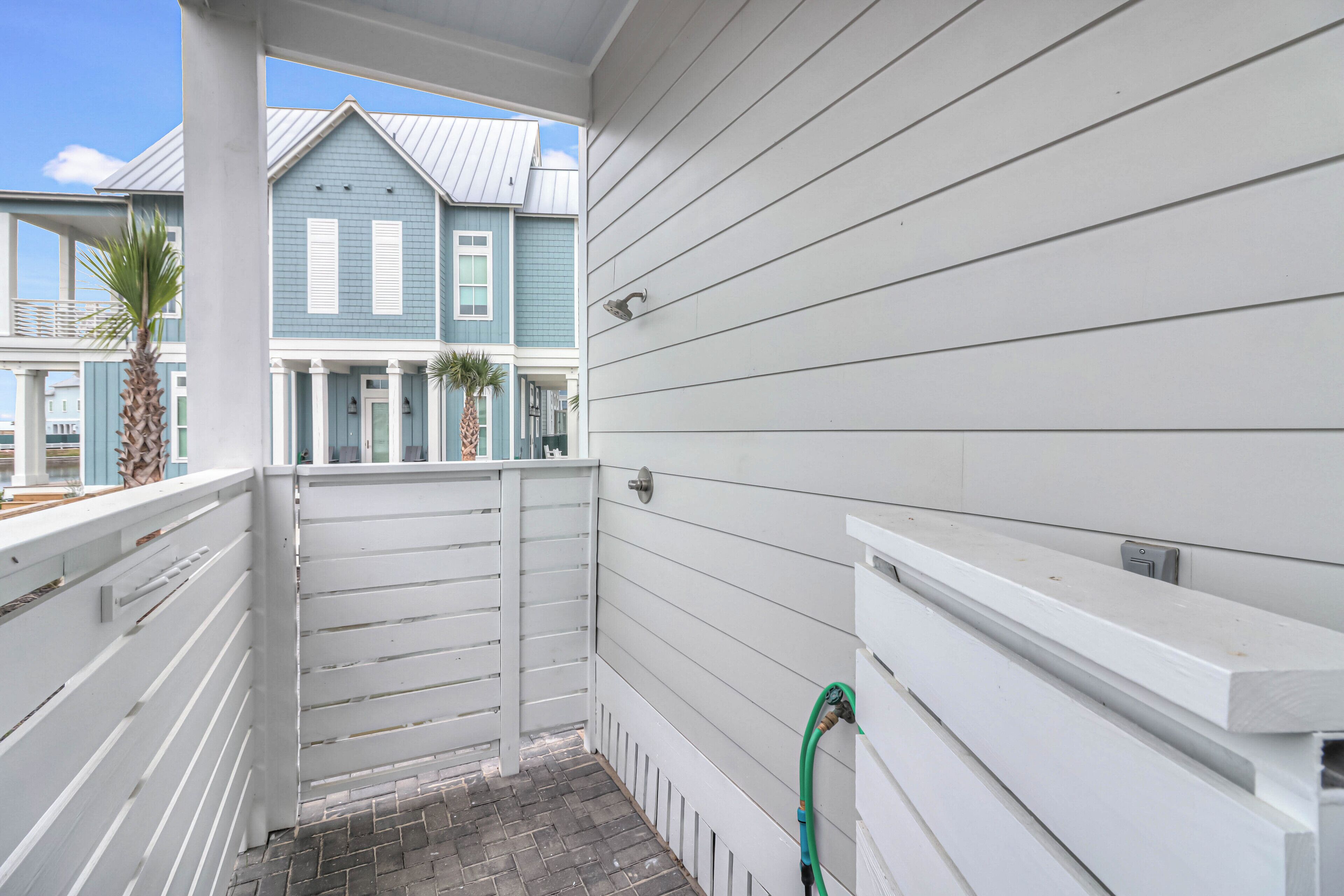 Een smal balkon met witte reling en een tegelvloer, met uitzicht op een rij huizen met blauwe bekleding en witte luiken.