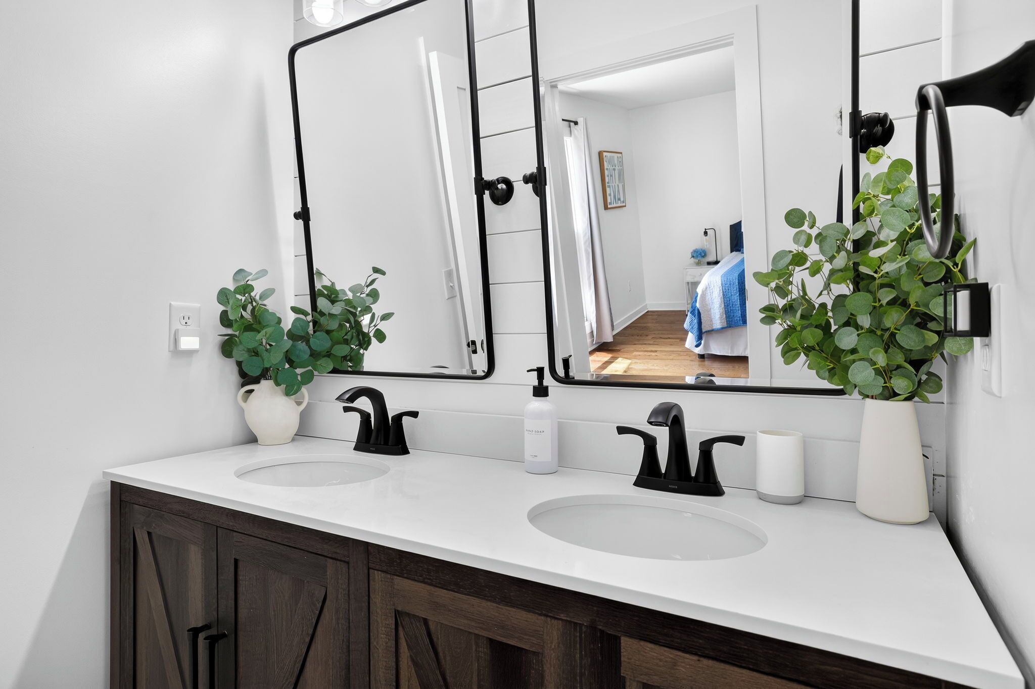 Un baño moderno con dos lavamanos, un espejo grande y plantas en macetas.