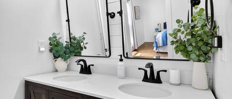 Un baño moderno con dos lavamanos, un espejo grande y plantas en macetas.