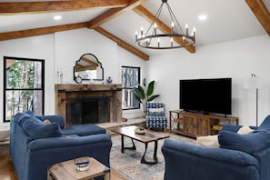 A living room with a fireplace, blue sofas, a television, and a chandelier. - Lakefront, Views, Private Dock, Boat Rental, Bunks, Near Clemson, Kayaks! (Starr)