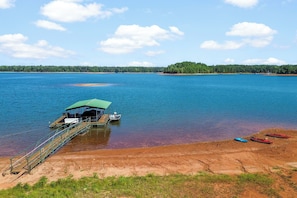 Um barco atracado em cais com área de estar coberta, rodeado por águas calmas e uma linha costeira arborizada.