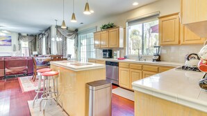 A modern kitchen with wooden cabinets, stainless steel appliances, and a central island with stools. - Outdoor Oasis + Hot Tub! Spacious Clovis Home (Clovis)